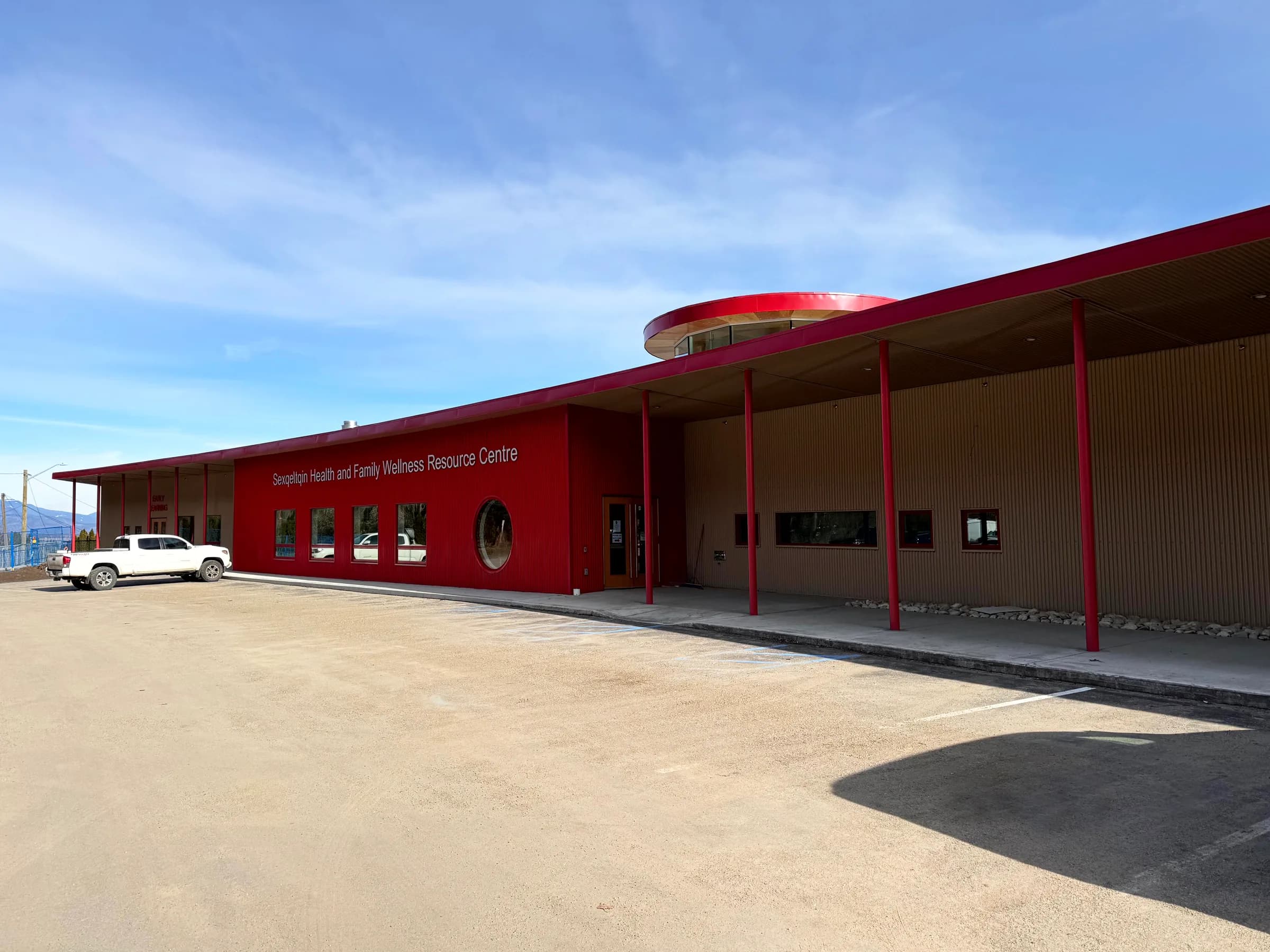 The completed centre, its long red elevation and slender red columns running beside the parking area below the hills.