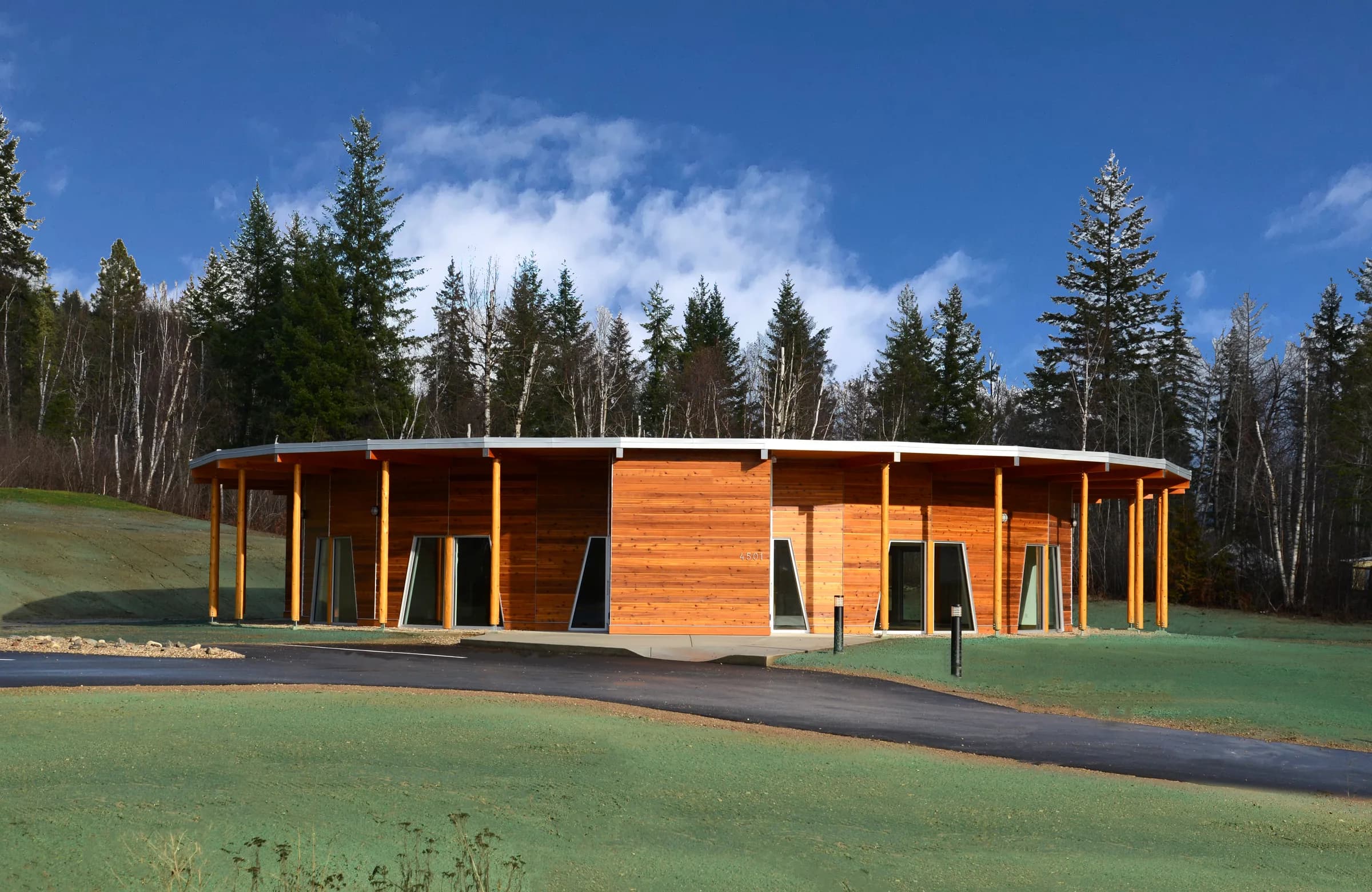 The completed childcare centre, its curved timber elevation and colonnade set into the sloping site among the trees.