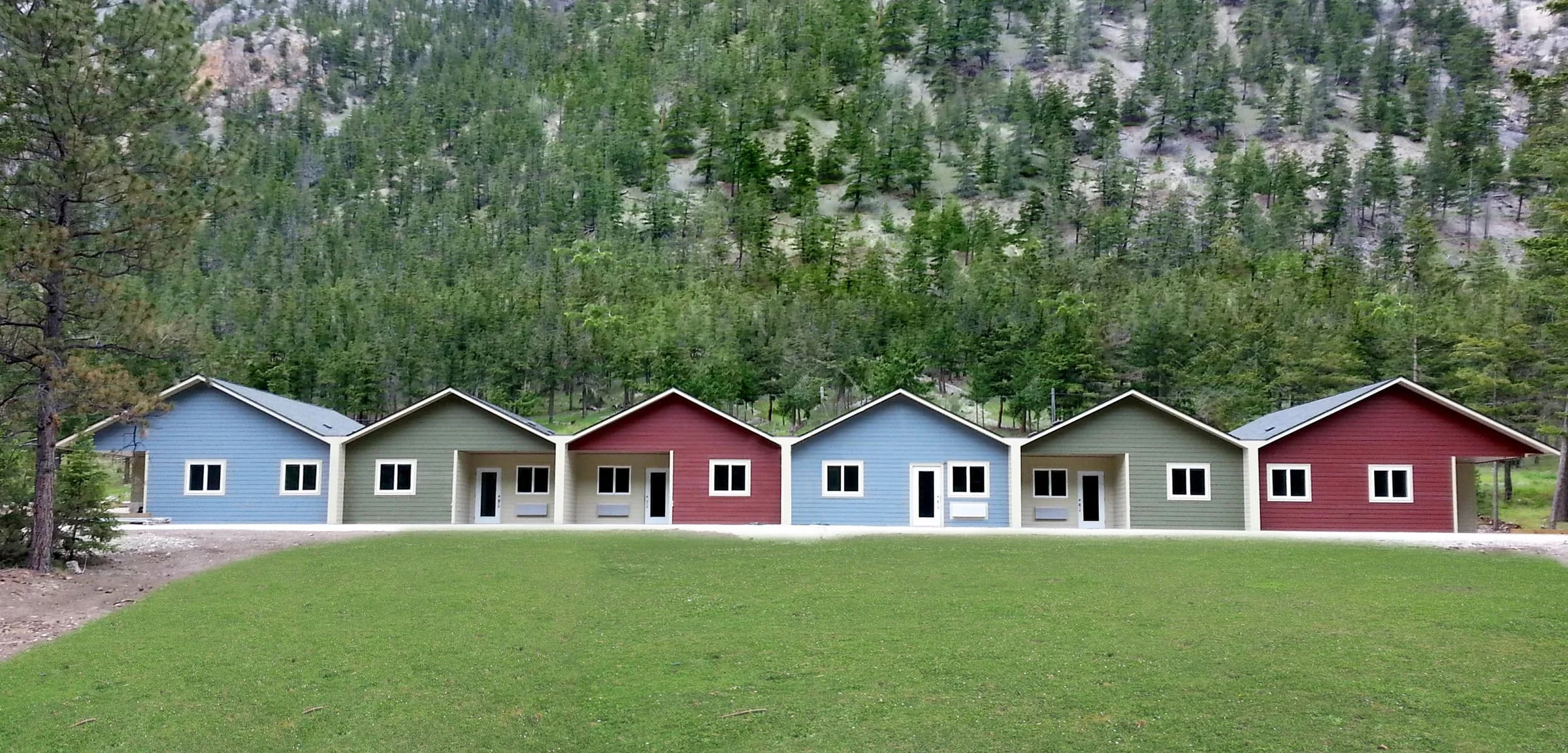 The completed row of Elders' housing units in blue, grey and red, set on the mountainside below the forest.