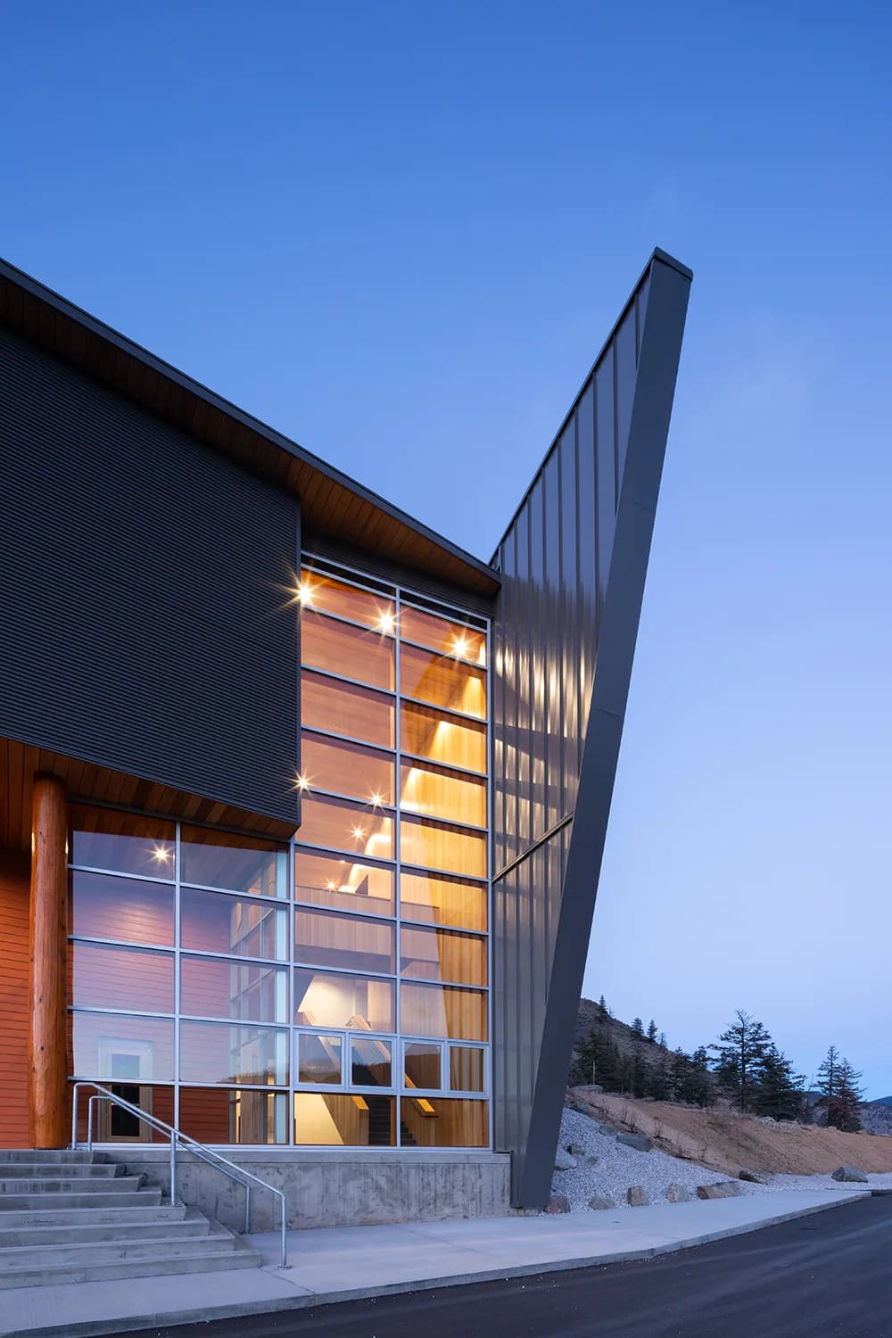 The glazed stair tower and cantilevered roof blade lit from within at dusk.